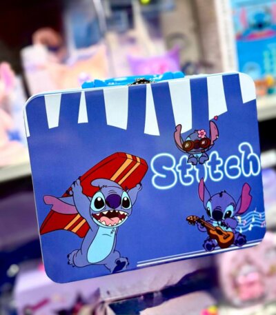 Valisette métallique de rangement bleu vif illustrée avec le personnage Disney Stitch dans trois poses : portant une planche de surf rouge, jouant de la guitare avec des notes de musique, et portant des lunettes de soleil roses avec une fleur. La boîte possède une poignée bleue et un fermoir en métal argenté.