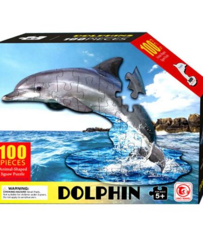 Boîte de puzzle rectangulaire montrant un dauphin gris en pièces de puzzle sautant au-dessus d'une mer bleue. Le texte indique "100 PIECES", "Animal-Shaped Jigsaw Puzzle", "DOLPHIN" et "FOR AGES 5+"