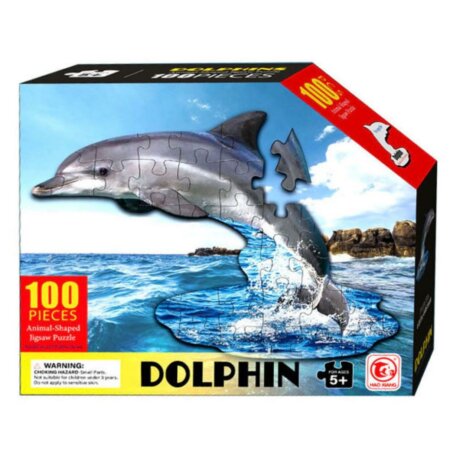 Boîte de puzzle rectangulaire montrant un dauphin gris en pièces de puzzle sautant au-dessus d'une mer bleue. Le texte indique "100 PIECES", "Animal-Shaped Jigsaw Puzzle", "DOLPHIN" et "FOR AGES 5+"