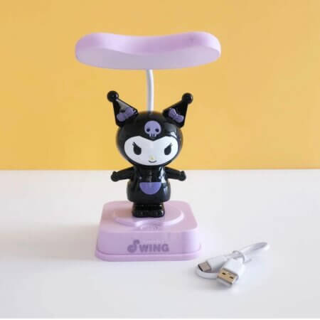 Lampe de table représentant la figurine Kuromi noire avec des détails violets, posée sur un socle tactile violet marqué "Joyful Swing". La lampe possède un abat-jour plat violet en hauteur et est accompagnée de son câble de recharge USB blanc.