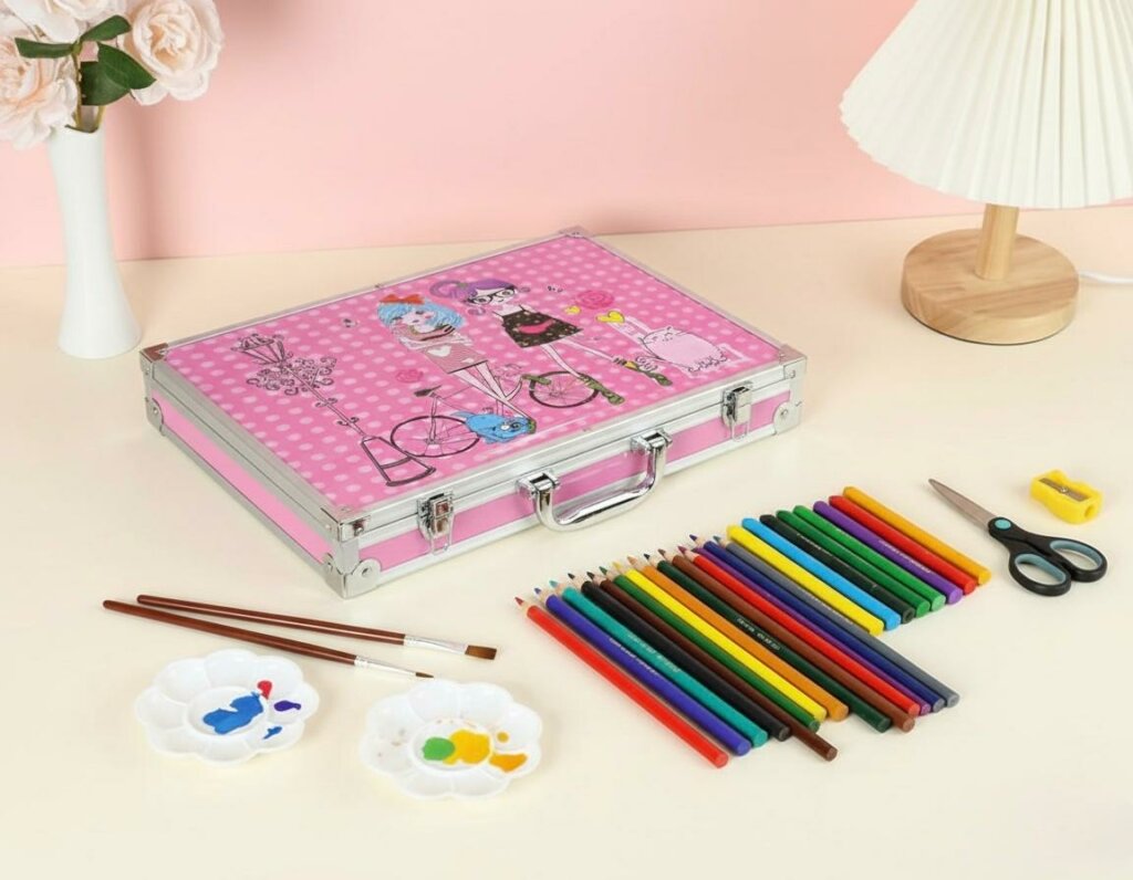 Coffret artistique en aluminium rose décoré d'illustrations de personnages, posé sur une table à côté d'une rangée de crayons de couleur, de pinceaux et de palettes de peinture