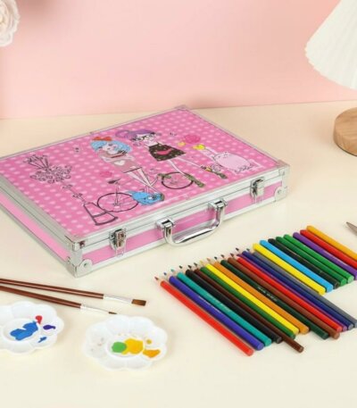 Coffret artistique en aluminium rose décoré d'illustrations de personnages, posé sur une table à côté d'une rangée de crayons de couleur, de pinceaux et de palettes de peinture