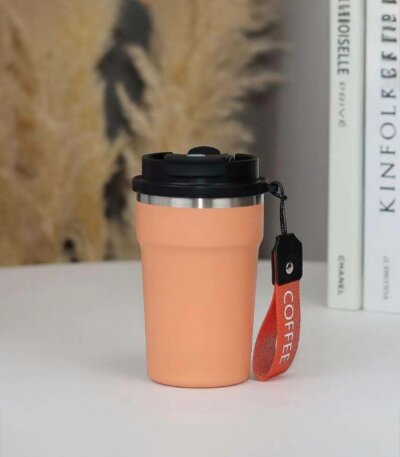 mug isotherme de voyage au design moderne et épuré. Le gobelet, de couleur pêche pastel, est doté d'une finition mate et d'une structure en acier inoxydable visible au niveau du bord supérieur.