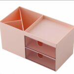 Organisateur de bureau en plastique rose pastel comprenant deux compartiments verticaux pour stylos, un plateau supérieur plat et deux tiroirs transparents superposés.