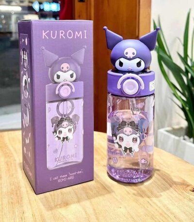 L'image montre une gourde réutilisable Kuromi (personnage de Sanrio) posée sur une table en bois clair, accompagnée de sa boîte d'emballage d'origine.Gourde Sanrio Kuromi avec Couvercle 3D et Paille.
