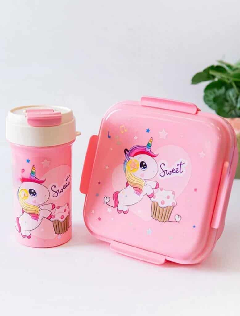 Une boîte à lunch carrée rose et une gourde assortie posées sur une surface blanche.