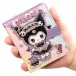 Gros plan sur un mini-carnet de notes violet et jaune à l'effigie du personnage Kuromi de Sanrio, tenu dans une main sur fond blanc.