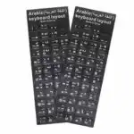 Deux planches rectangulaires d'autocollants noirs pour clavier d'ordinateur sont posées côte à côte sur un fond blanc uni. Chaque planche comporte un en-tête noir avec l'inscription « Arabic (اللغة العربية) keyboard layout » et la mention « Made in China » écrites en blanc. Les autocollants individuels correspondent aux touches d'un clavier standard et affichent des caractères blancs, combinant des lettres de l'alphabet latin (disposition QWERTY), des chiffres et des caractères de l'alphabet arabe.