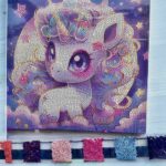 Toile de broderie diamant représentant une petite licorne violette de style manga kawaii, accompagnée de ses sachets de strass colorés prêts pour la création.