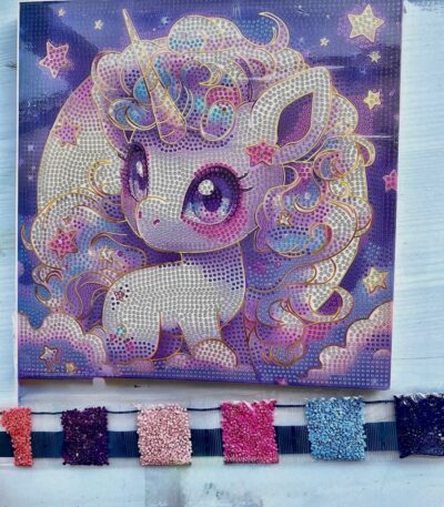 Toile de broderie diamant représentant une petite licorne violette de style manga kawaii, accompagnée de ses sachets de strass colorés prêts pour la création.