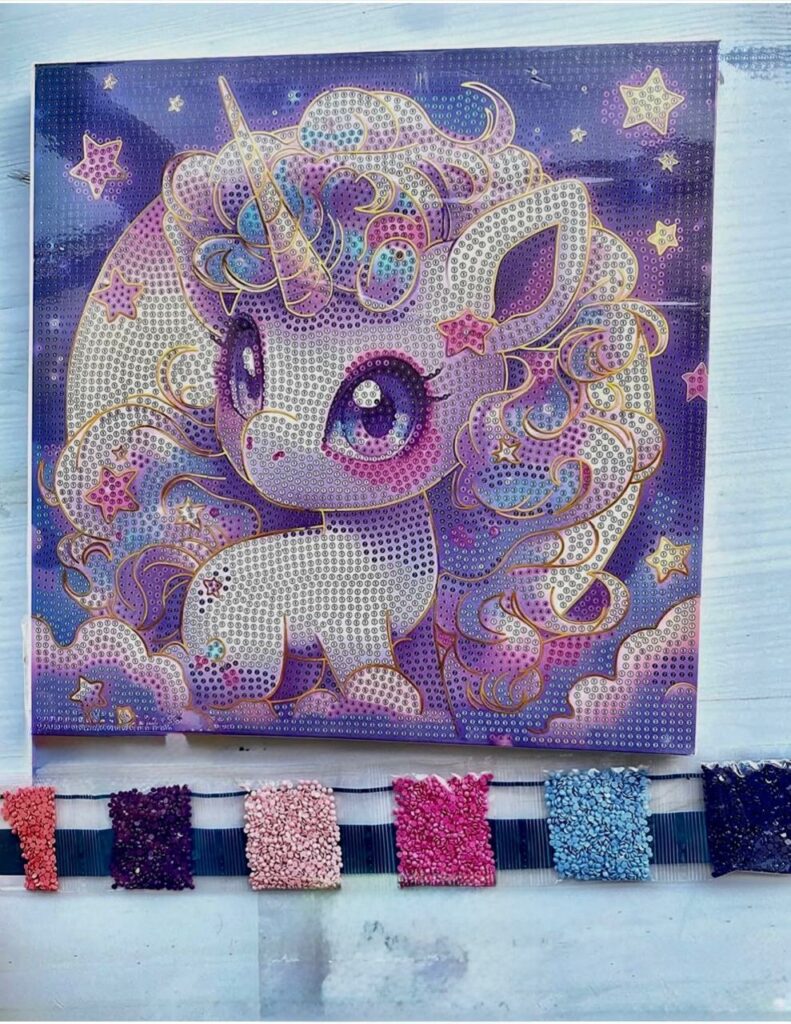 Toile de broderie diamant représentant une petite licorne violette de style manga kawaii, accompagnée de ses sachets de strass colorés prêts pour la création.