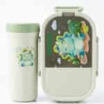 Ensemble de repas pour enfant comprenant une boîte à déjeuner ovale et une gourde assortie de couleur blanc cassé et vert menthe. Le couvercle de la boîte et le devant de la gourde sont décorés d'un petit tricératops bleu rigolo entouré de cactus
