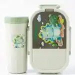 Ensemble de repas pour enfant comprenant une boîte à déjeuner ovale et une gourde assortie de couleur blanc cassé et vert menthe. Le couvercle de la boîte et le devant de la gourde sont décorés d'un petit tricératops bleu rigolo entouré de cactus