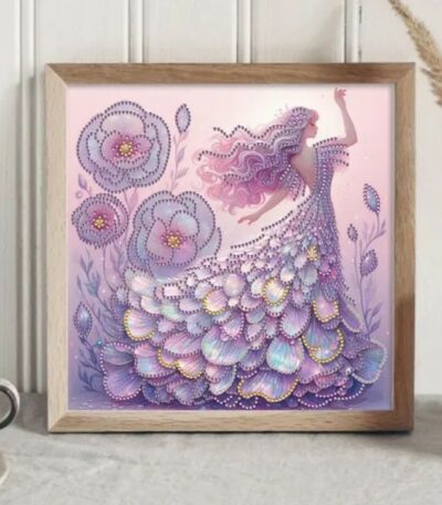 Un tableau carré encadré de bois clair présente une broderie diamant dans les tons violets et lavande. Une femme élégante est représentée de profil, un bras levé, arborant de longs cheveux roses ondulés. Elle porte une robe de bal somptueuse et volumineuse, faite de strass scintillants superposés en forme de pétales ou de plumes aux reflets nacrés. Sur la gauche, de grandes fleurs violettes stylisées et ornées de perles brillantes complètent cette scène féerique.