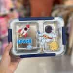 Une boîte à lunch rectangulaire à deux compartiments avec un couvercle transparent orné de motifs spatiaux