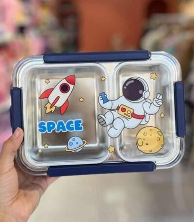 Une boîte à lunch rectangulaire à deux compartiments avec un couvercle transparent orné de motifs spatiaux : un astronaute, une fusée rouge et blanche, une lune jaune et des petites étoiles