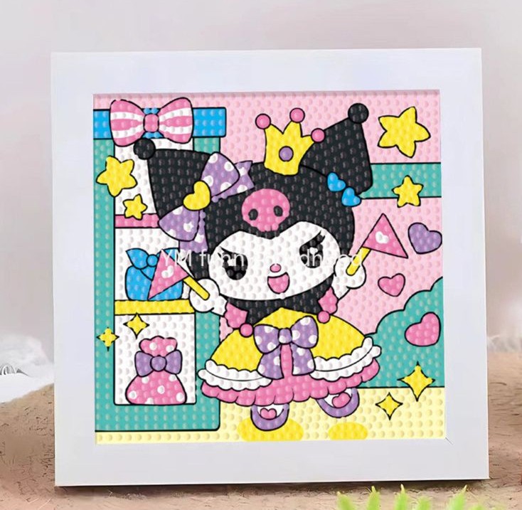 Un kit de broderie diamant terminé et encadré dans un cadre blanc carré posé sur une surface texturée. La toile montre le personnage Kuromi de Sanrio habillée en princesse. Elle porte sa coiffe noire à tête de mort rose surmontée d'une petite couronne jaune, une robe de bal jaune et rose avec un nœud papillon violet à pois blancs, et des chaussures violettes. Kuromi sourit, lève les bras et tient une baguette magique rose. À gauche, une étagère turquoise contient un nœud papillon rose, un flacon bleu et un parfum rose. L'arrière-plan est rose clair à pois blancs, décoré d'étoiles jaunes et de cœurs roses. Toute l'illustration est entièrement recouverte de strass ronds en relief qui donnent un effet texturé et brillant.