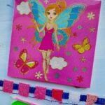 Kit de broderie diamant représentant une fée aux ailes de papillon bleues sur un fond rose vif, accompagné de ses strass colorés et de ses outils de pose.