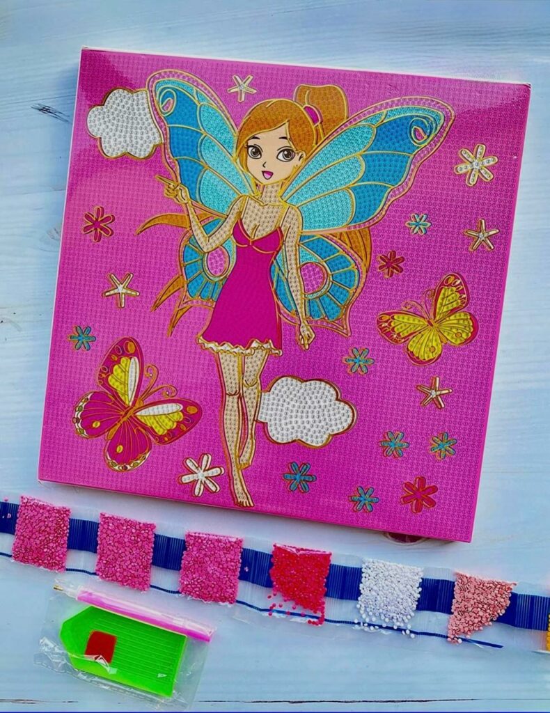 Kit de broderie diamant représentant une fée aux ailes de papillon bleues sur un fond rose vif, accompagné de ses strass colorés et de ses outils de pose.