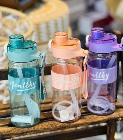 Trois gourdes de sport transparentes de la marque Healthy, déclinées en bleu turquoise, orange pêche et violet. Elles disposent d'un manchon en silicone strié assorti, d'une sangle de transport et d'une paille blanche visible à l'intérieur.
