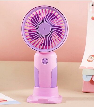 Un mini ventilateur portable rechargeable bicolore, violet et rose, posé à la verticale sur son socle de table rose assorti. Le manche présente un design ergonomique rose avec des inserts violets sur les côtés et un bouton d'alimentation rond au centre.