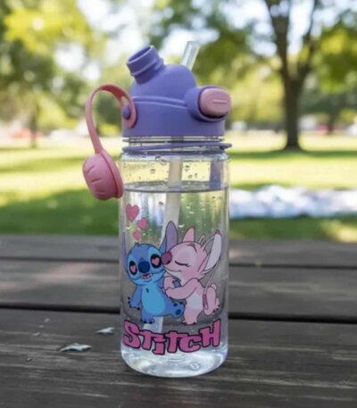 Gourde pour enfants transparente avec motif de Stitch et Angel de Disney s'embrassant avec des cœurs roses. La bouteille possède un bouchon violet avec une paille intégrée transparente déployée, un bouton-poussoir rose et une poignée souple en silicone rose, posée à l'extérieur sur une table de pique-nique en bois.