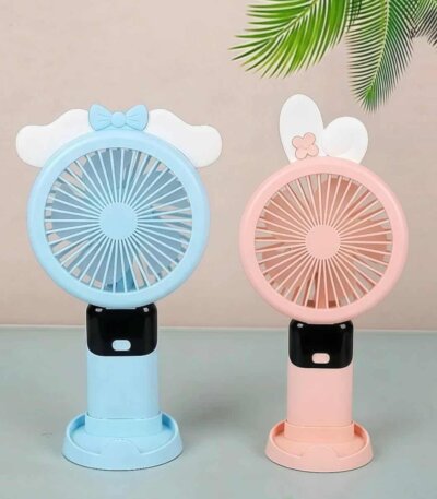 Deux mini ventilateurs portables rechargeables au design mignon, posés côte à côte sur une surface plane vert clair. À gauche, un modèle bleu clair est décoré sur le dessus d'un nœud papillon bleu posé sur de petites ailes blanches.
