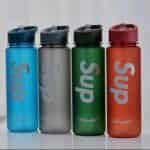 L'image montre des bouteilles d'eau de sport de la marque "Sup", reconnaissables à leur fini dépoli et aux inscriptions "Sup" et "Beautiful" sur le corps de la bouteille