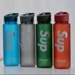 L'image montre des bouteilles d'eau de sport de la marque "Sup", reconnaissables à leur fini dépoli et aux inscriptions "Sup" et "Beautiful" sur le corps de la bouteille