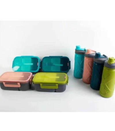 Une collection de quatre kits de repas coordonnés, disposés sur un fond blanc uni. À gauche, quatre boîtes à lunch rectangulaires à compartiments sont alignées sur deux rangées ; elles possèdent des couvercles translucides colorés (bleu turquoise, vert sapin, rose corail et vert olive) avec des clips de fermeture latéraux et une cuillère intégrée visible sur le dessus
