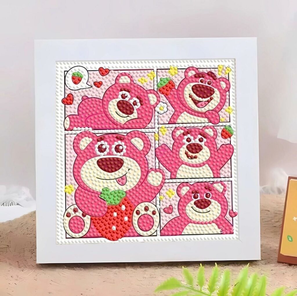 Un kit de broderie diamant terminé et encadré, représentant le personnage de l'ours Lotso de Toy Story dans un style bande dessinée. Le tableau carré est divisé en cinq cases montrant l'ours rose dans différentes poses mignonnes : allongé, agitant la main, tenant une grosse fraise rouge, ou souriant. Le fond de chaque case utilise des couleurs pastel (blanc, jaune, rose) décorées de petites fraises et de cœurs. Toute la surface du dessin est recouverte de strass ronds en relief bien alignés qui scintillent