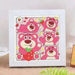 Un kit de broderie diamant terminé et encadré, représentant le personnage de l'ours Lotso de Toy Story dans un style bande dessinée. Le tableau carré est divisé en cinq cases montrant l'ours rose dans différentes poses mignonnes : allongé, agitant la main, tenant une grosse fraise rouge, ou souriant. Le fond de chaque case utilise des couleurs pastel (blanc, jaune, rose) décorées de petites fraises et de cœurs. Toute la surface du dessin est recouverte de strass ronds en relief bien alignés qui scintillent