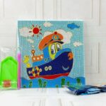 Un kit de broderie diamant pour enfants présenté sur une surface en bois blanc devant un mur en briques blanches. La toile carrée au centre montre une illustration enfantine d'un avion orange anthropomorphe avec de grands yeux expressifs. L'avion vole dans un ciel bleu vif parsemé de petits nuages blancs texturés de cercles. En bas du dessin, on aperçoit des collines vertes et des arbres stylisés. À gauche de la toile se trouve un sachet transparent contenant les outils de pose : un plateau de tri vert, un stylet rose et un carré de cire rouge.