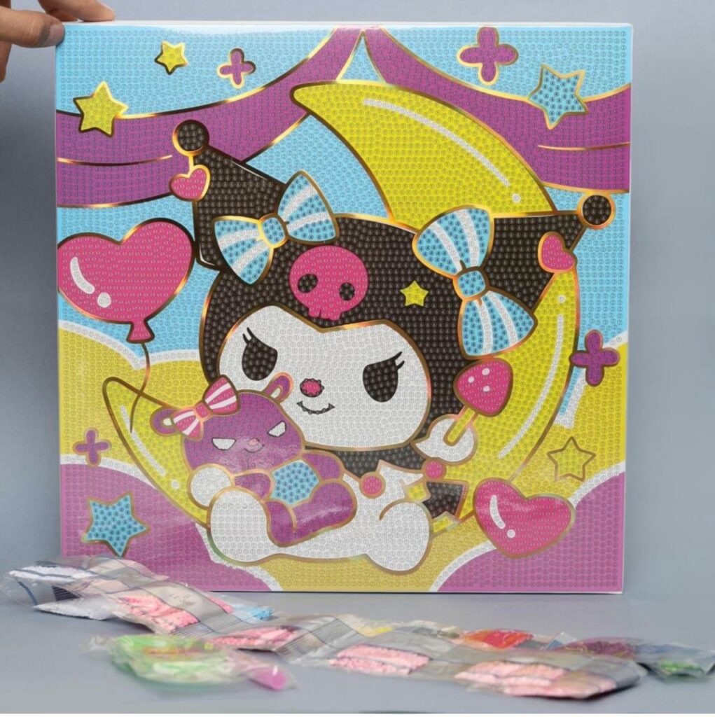 Un kit de broderie diamant représentant le personnage Kuromi de Sanrio. La toile carrée montre Kuromi avec sa coiffe noire à tête de mort rose, assise sur un croissant de lune jaune vif et tenant une petite peluche violette. L'arrière-plan est décoré d'étoiles, de cœurs roses et de vagues de couleurs pastel violettes et bleues. Toute la surface est recouverte de petits cercles numérotés prêts à recevoir les strass. Au premier plan, au pied de la toile posée à la verticale, se trouvent plusieurs sachets plastiques transparents alignés contenant les diamants colorés (rose, blanc, vert, violet).