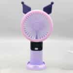 Un mini ventilateur portable rechargeable de couleur violette et mauve, inspiré du personnage Kuromi de Sanrio, posé verticalement sur son socle de table assorti. La tête ronde possède une grille rose-mauve surmontée de deux oreilles pointues de bouffon violet foncé. Le manche intègre un écran numérique noir affichant le chiffre « 5 » en bleu juste au-dessus d'un bouton d'alimentation blanc.