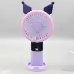 Un mini ventilateur portable rechargeable de couleur violette et mauve, inspiré du personnage Kuromi de Sanrio, posé verticalement sur son socle de table assorti. La tête ronde possède une grille rose-mauve surmontée de deux oreilles pointues de bouffon violet foncé. Le manche intègre un écran numérique noir affichant le chiffre « 5 » en bleu juste au-dessus d'un bouton d'alimentation blanc.