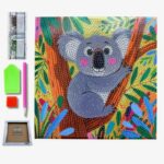 Un kit complet de broderie diamant pour enfants présenté sur fond blanc. La toile carrée au centre montre une illustration colorée et enfantine d'un koala gris assis sur la branche d'un arbre. Le koala a de grands yeux ronds, des joues roses et un grand nez noir. Il est entouré de feuilles tropicales stylisées vertes, jaunes, rouges et bleues. Toute la surface du dessin est recouverte de petits cercles pour guider la pose des strass. À gauche de la toile se trouvent les accessoires inclus : une rangée verticale de sachets de diamants colorés, un plateau de tri vert, un carré de cire rouge, un stylet applicateur rose et, tout en bas, un petit cadre de présentation en bois de la marque "Seven Hobbies".