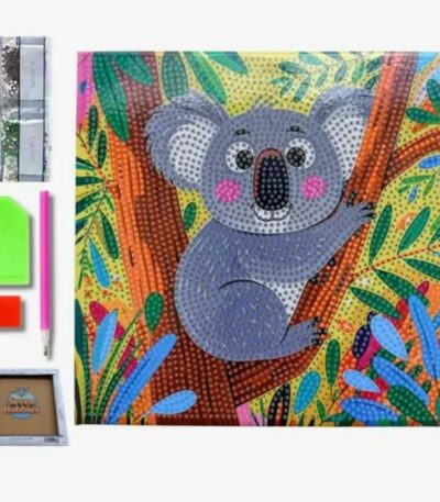 Un kit complet de broderie diamant pour enfants présenté sur fond blanc. La toile carrée au centre montre une illustration colorée et enfantine d'un koala gris assis sur la branche d'un arbre. Le koala a de grands yeux ronds, des joues roses et un grand nez noir. Il est entouré de feuilles tropicales stylisées vertes, jaunes, rouges et bleues. Toute la surface du dessin est recouverte de petits cercles pour guider la pose des strass. À gauche de la toile se trouvent les accessoires inclus : une rangée verticale de sachets de diamants colorés, un plateau de tri vert, un carré de cire rouge, un stylet applicateur rose et, tout en bas, un petit cadre de présentation en bois de la marque "Seven Hobbies".