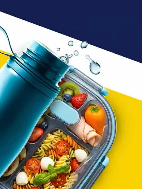 Vue de dessus d'une gourde réutilisable bleu canard à côté d'une lunch box compartimentée contenant une salade de pâtes, des tranches de kiwi, des fraises, des myrtilles et des roulés de dinde sur un fond blanc épuré.